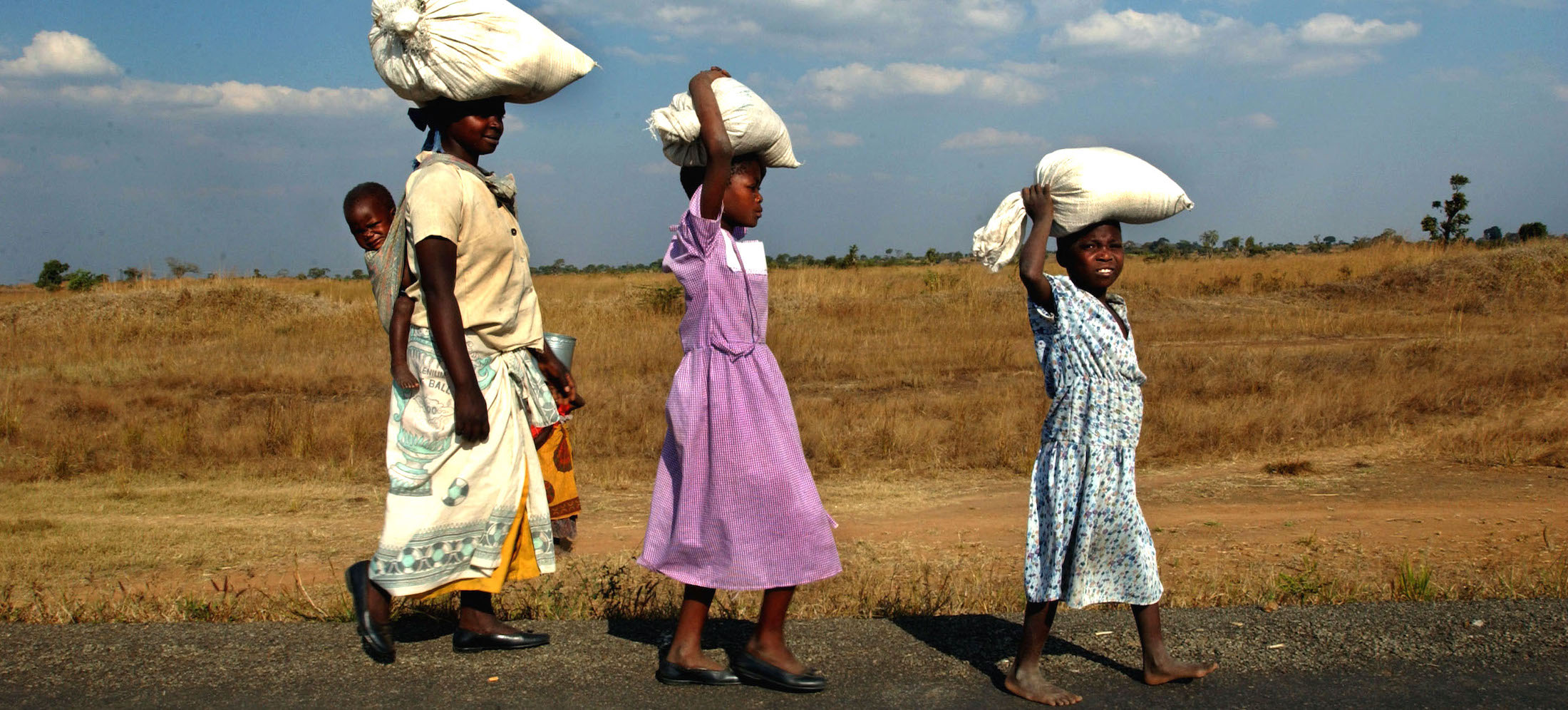 Mother and her two children carry bags of rice on their heads