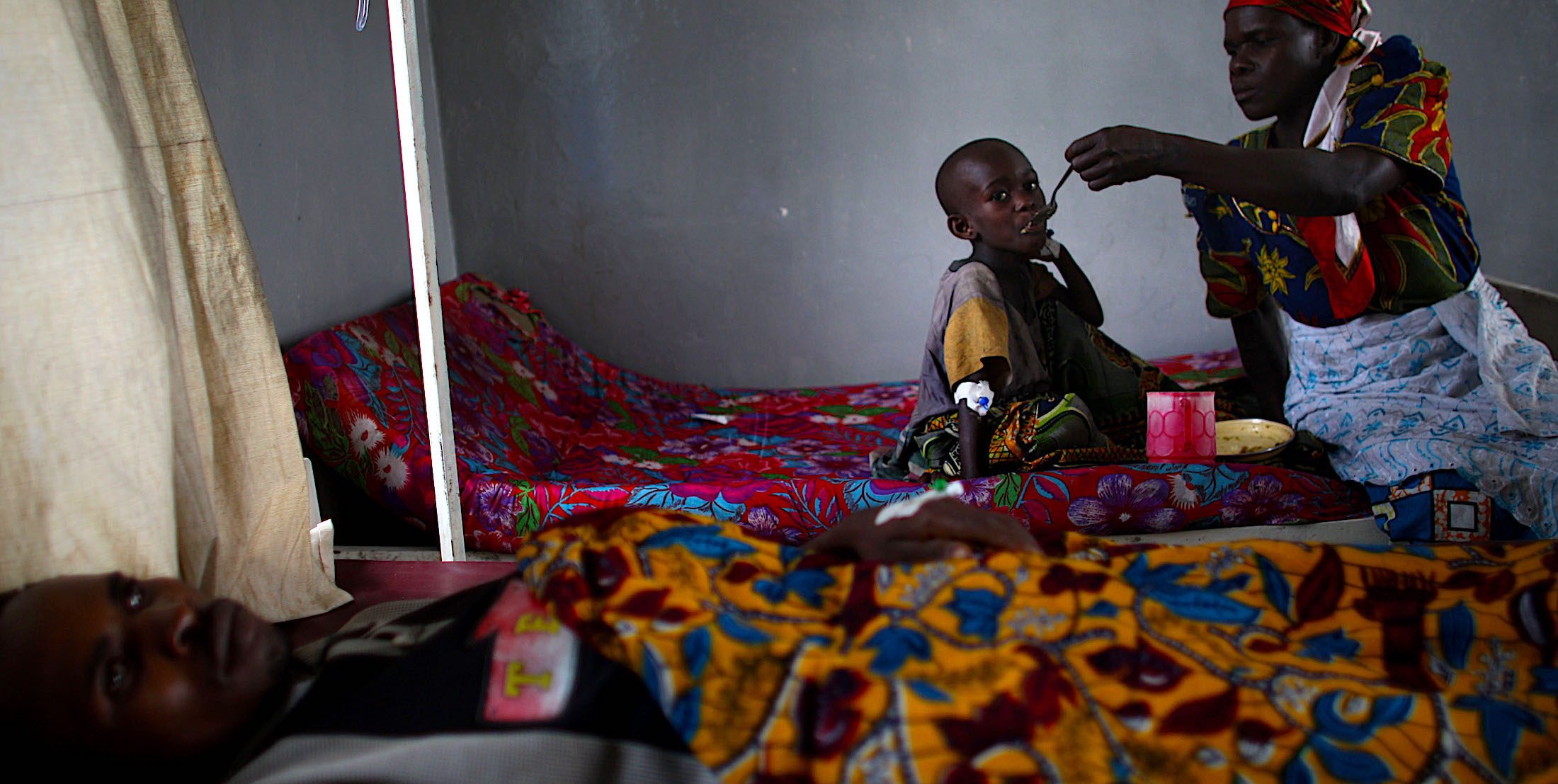 A women and child sitting on bed and the women is feeding the child
