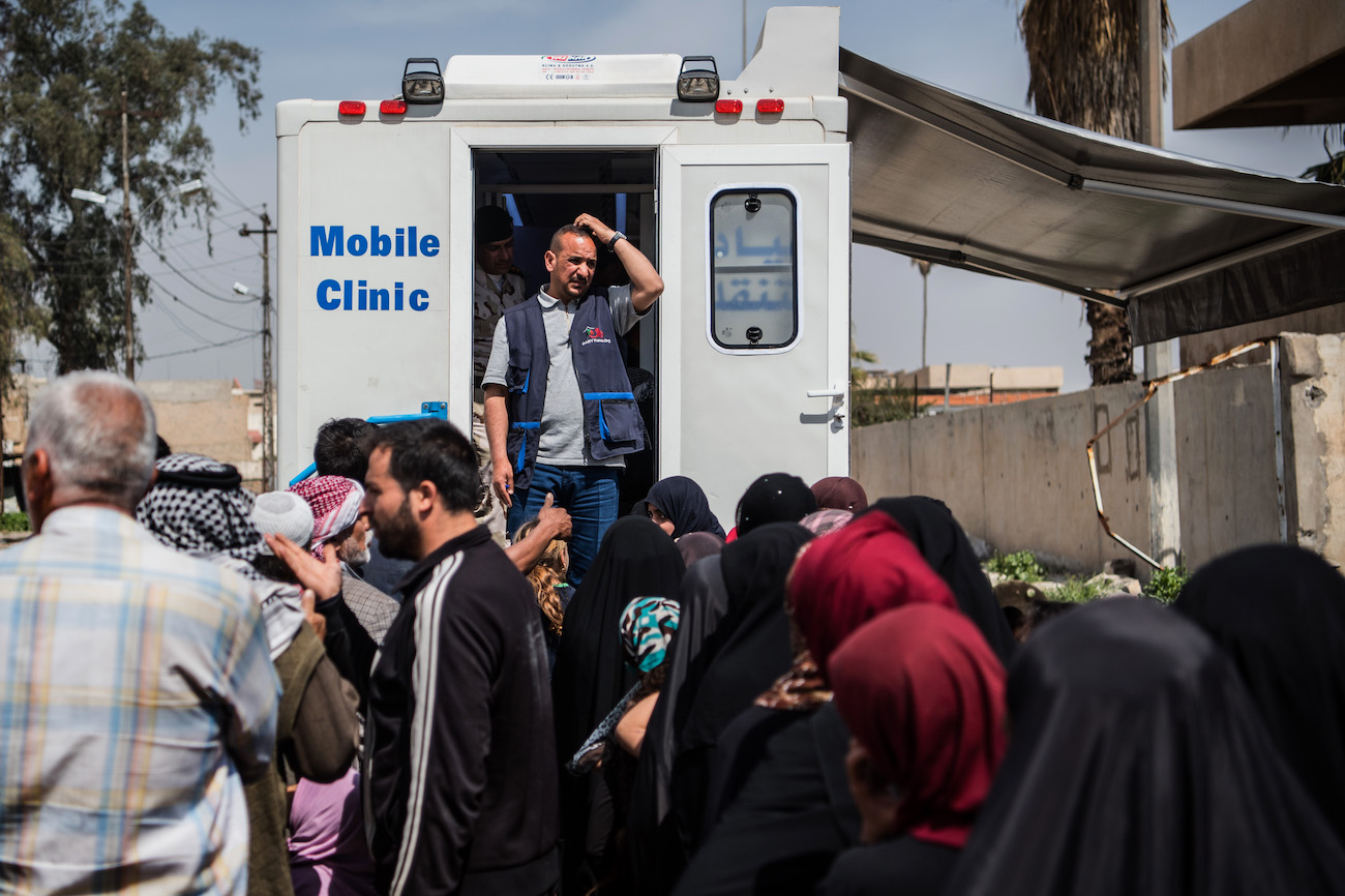 A solitary aid worker looks on as people queue for treatment from his mobile clinic during fighting in Iraq in 2017