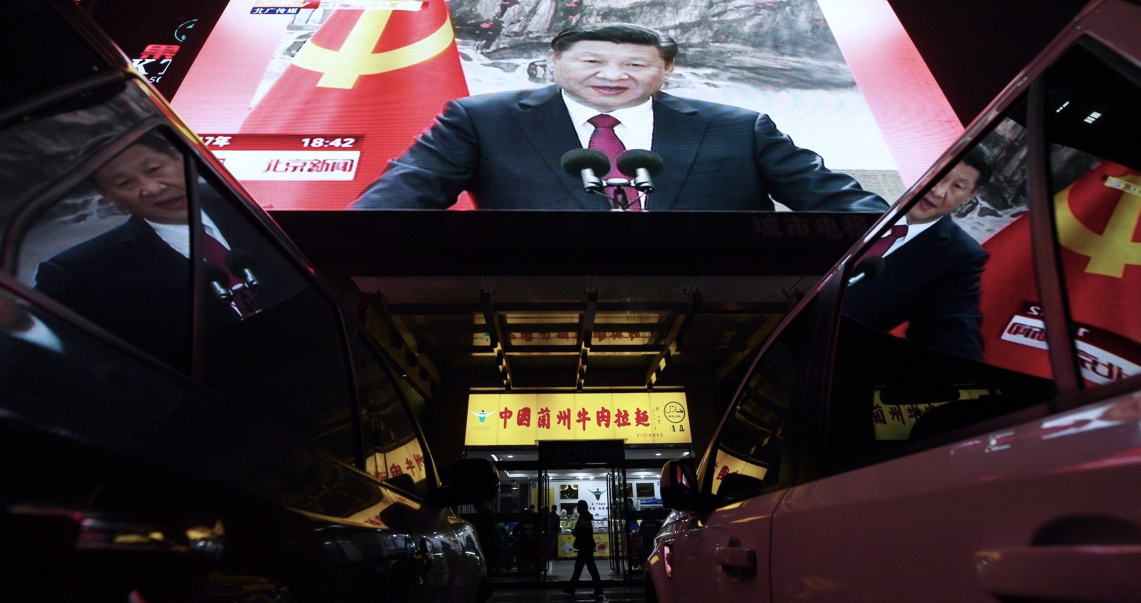 People walk below a screen showing news coverage about Chinese President Xi Jinping. | Greg Baker/AFP via Getty Images