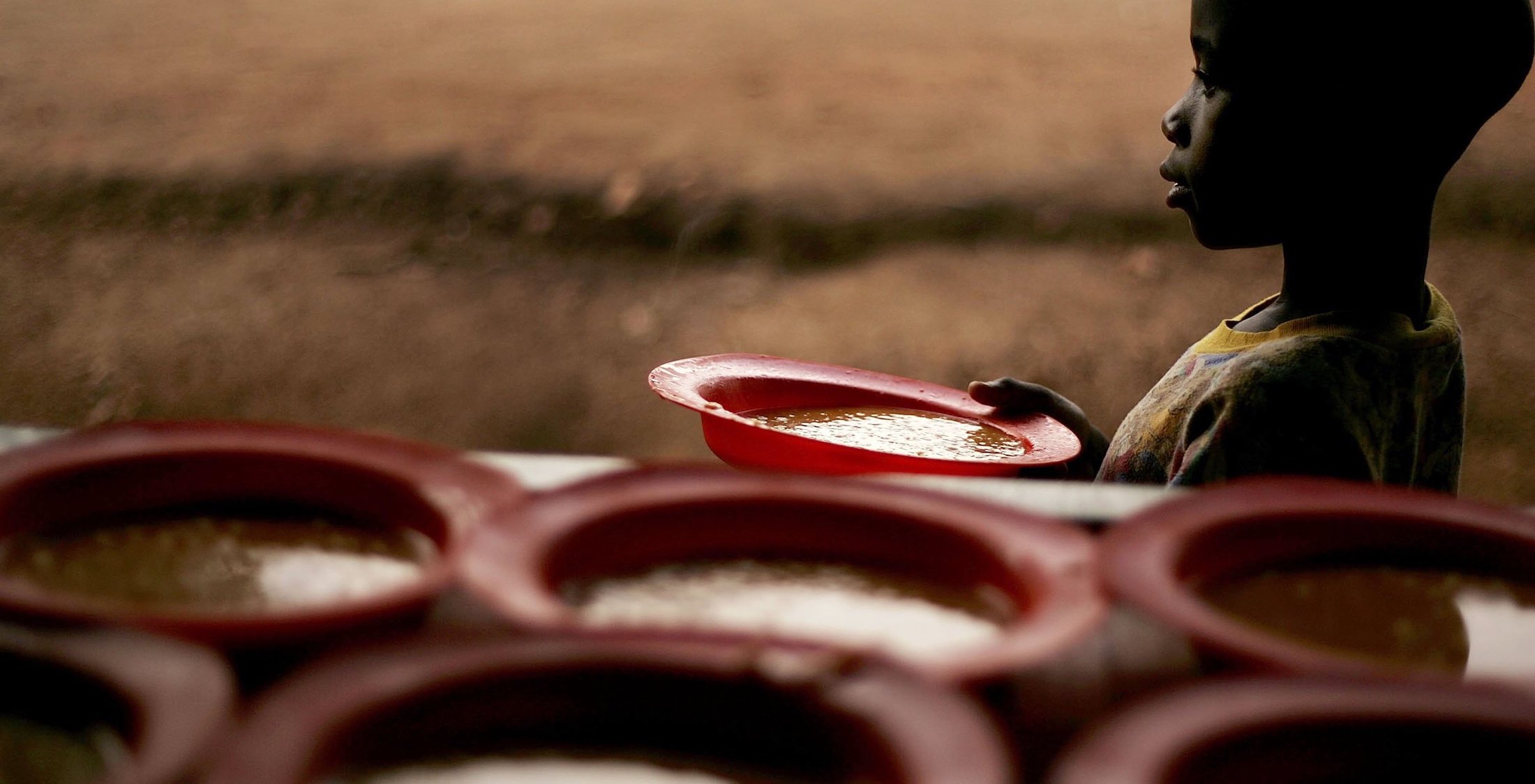 Young child taking a bowl of soup from a table that has many bowls of soup