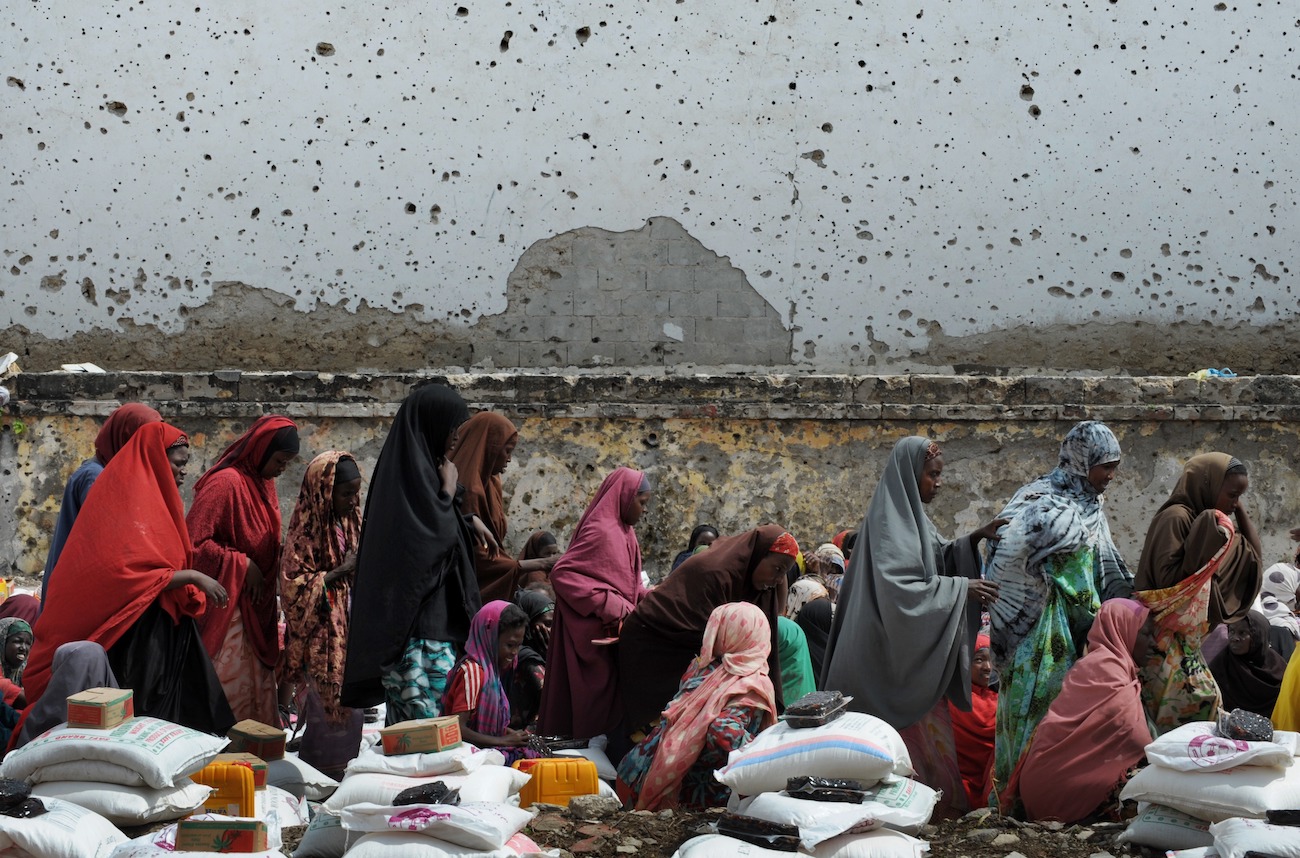 Somali women who fled drought and violence wait beneath a bullet scarred wall to collect aid