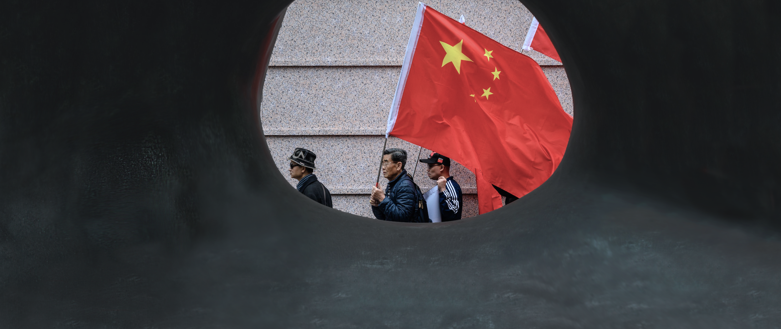 Pro-China protestors march down the street holding the Chinese flag. | Anthony Wallace/AFP via Getty Images