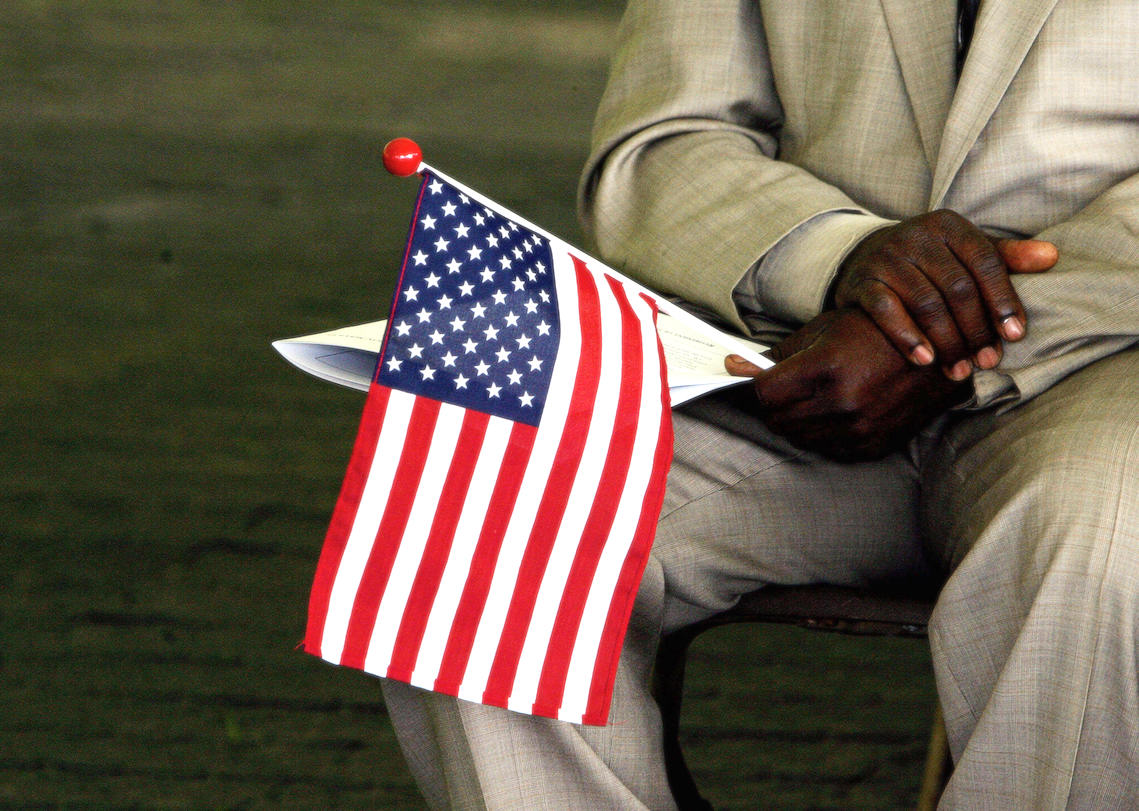 A man originally from Sierra Leone holds a US flag while waiting to become a US citizen during a naturalization ceremony in 2006. | JIM WATSON/AFP via Getty Images