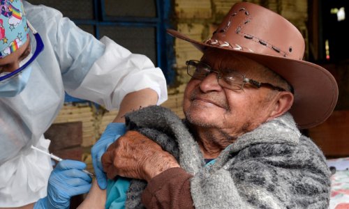A nursing assistant gives a 95-year-old Colombian man his second dose of the Sinovac COVID shot. The man winces from the needle injection.