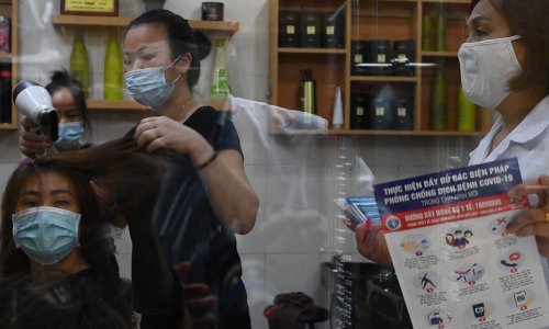 A stylist blow drys a woman's hair in Hanoi while a local health officer advises her to close.