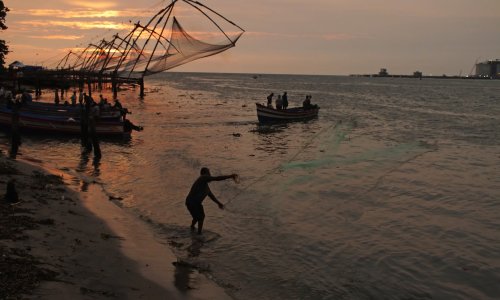 A man casts a fishing net in the sunset.