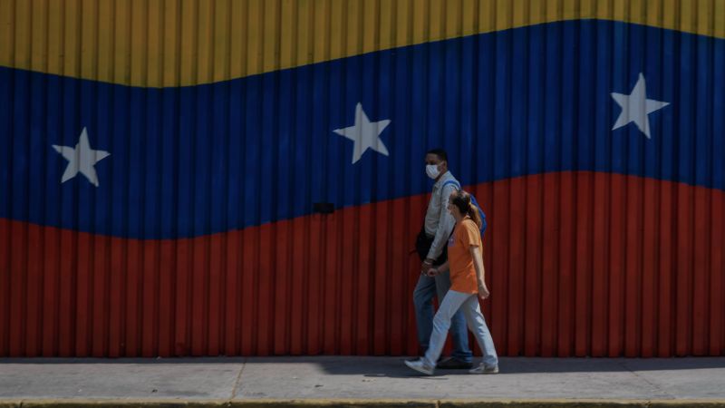 A couple wearing face masks walks past a wall painted as the Venezuelan national flag in Caracas on April 17, 2020, amid the novel coronavirus (COVID-19) outbreak. | FEDERICO PARRA/AFP via Getty Images