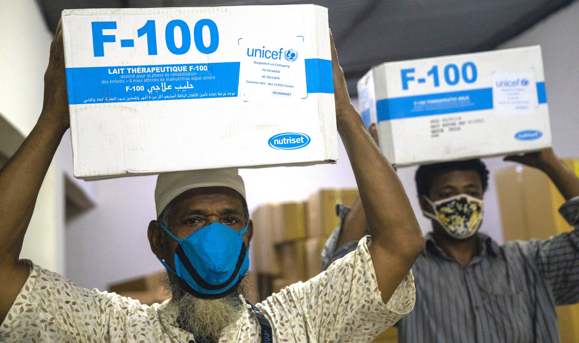 Transport workers in Bangladesh wearing face masks unload UNICEF nutrition kits filled with therapeutic milk for children with severe acute malnutrition. | Habibul Haque/UNICEF