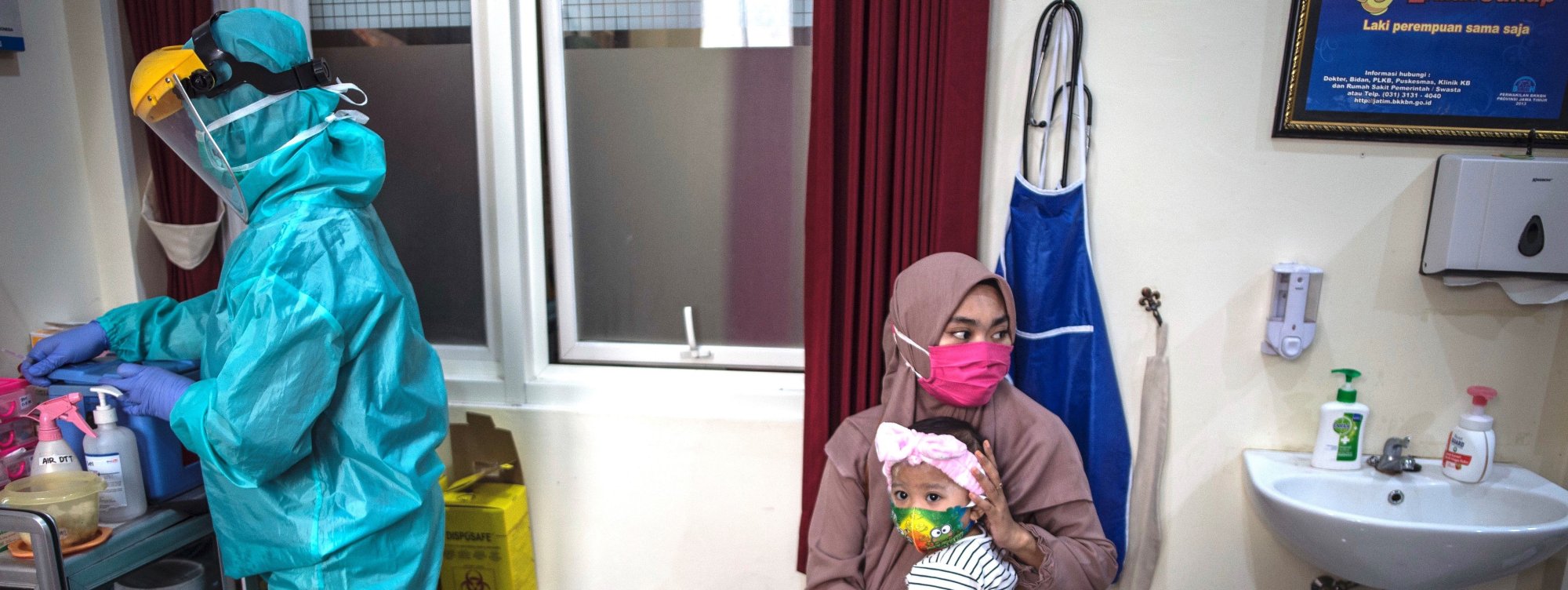 A woman holds her baby as a medical staff clad in protective gear prepares the Bacillus CalmetteGuérin (BCG) vaccine for tuberculosis and oral polio vaccine at a community health centre in Surabaya on June 30, 2020.