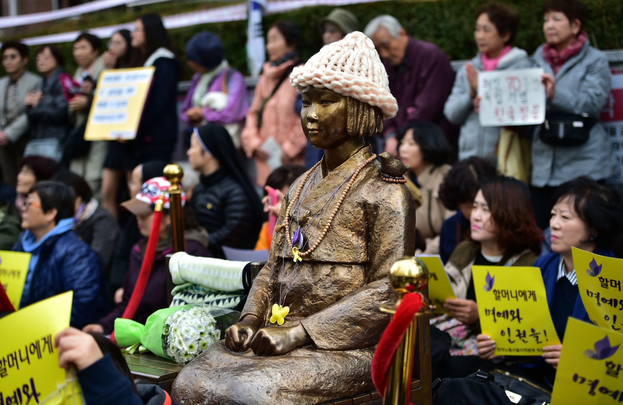 Protesters sit next to a statue of a South Korean teenage girl in traditional costume honoring former comfort women on November 11, 2015. (Photo by JUNG YEON-JE/AFP via Getty Images.)