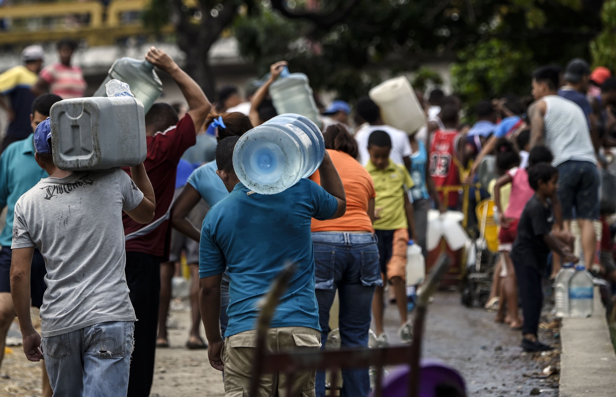Caption: People carry cans and buckets to collect water from a broken pipe, flowing into a sewage canal at the Guaire river in Caracas on March 11, 2019, as a massive power outage continues affecting some areas of the country.